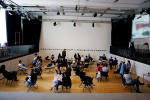 A group of people are sitting on chairs in a large room and chatting.